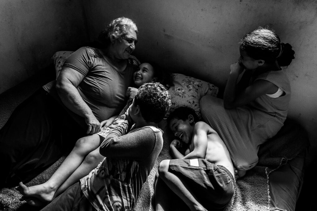 Caption: Sandra Mara Siqueira rests with her grandchildren, Micael, Davi, Ana Flávia, and Vitória. Living in the Parque dos Lagos occupation since 2013, the family seeks land regularization to guarantee access to basic infrastructure. Colombo, Paraná, Brazil, 15 November 2025 Story: Millions of Brazilians lack safe and affordable housing, with a national shortage of 5.9 million homes forcing approximately 16.4 million people into informal settlements. In the city of Colombo, the Parque dos Lagos occupation is home to 200 families living without official access to water, sewage disposal, or electricity. This project examines the struggle for land regularization, the legal process of converting informal possession into property rights. For Sandra Mara Siqueira and these communities, legal tenure is the essential gateway to credit, permanence, and dignity.
